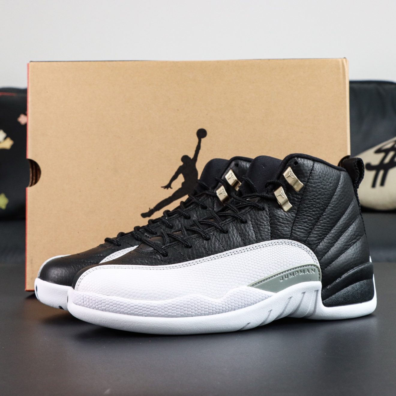 Jordan 12 Playoffs reps with black leather upper and white outsole beside box